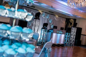 A wedding venue is decorated in a blue and silver theme. The wedding DJ setup looks stunning with colour coded venue uplighting to match.