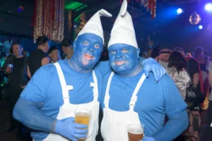 2 friends in fancy dress wearing blue face paint at charity party. Disco lights and DJ in the background.