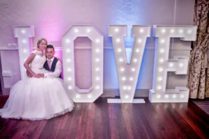 5 foot Light up LOVE letters with bride and groom sitting on them. Venue uplighting projects blue and pink light.