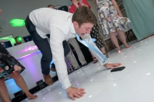 Wedding reception guest performs wiggly worm breakdance move on our starlit LED dance floor. The DJ plays music in the background.