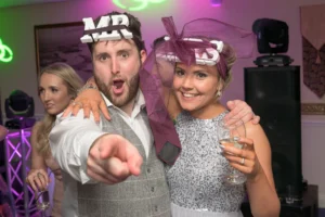 Bride and groom wear Mr and Mrs signs on their heads for party picture. A mobile disco is playing music in the background.