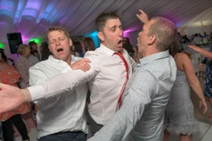 Wedding guests are celebrating at a reception in a marquee. Beautiful uplighting in pink, green and blue accentuate the party atmosphere.