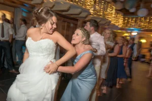 The bride leads a conga dance chain at a beautiful rustic wedding reception decorated with string lights. Everybody is having fun.