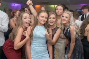 Promenade dance party disco. Young ladies are posing for a selfie. The crowd is having a good time whilst the DJ plays music.